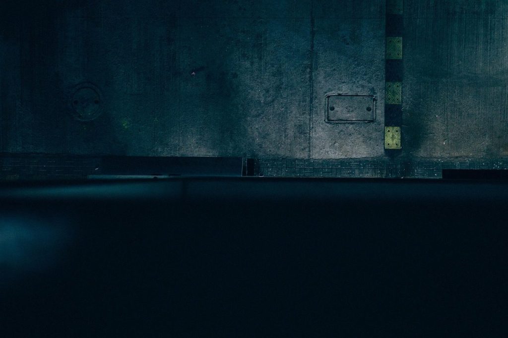 A weathered concrete wall over still water, lit teal