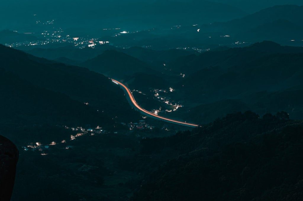 A lit road threading through dark hills at night