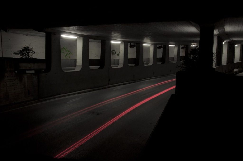 A single tail light traced through an unlit road underpass