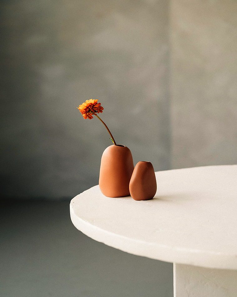Simple ceramic vases with a single orange flower on a table, minimalist style