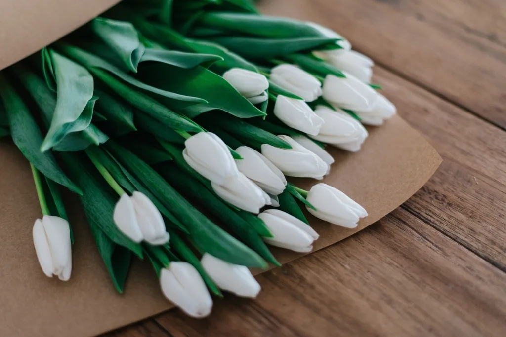 White tulips half wrapped in kraft paper on the workbench.