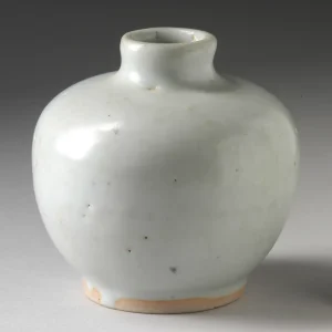 A small white ceramic vase standing empty on a pale surface.