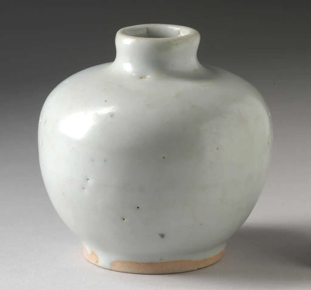 A small white ceramic vase standing empty on a pale surface.
