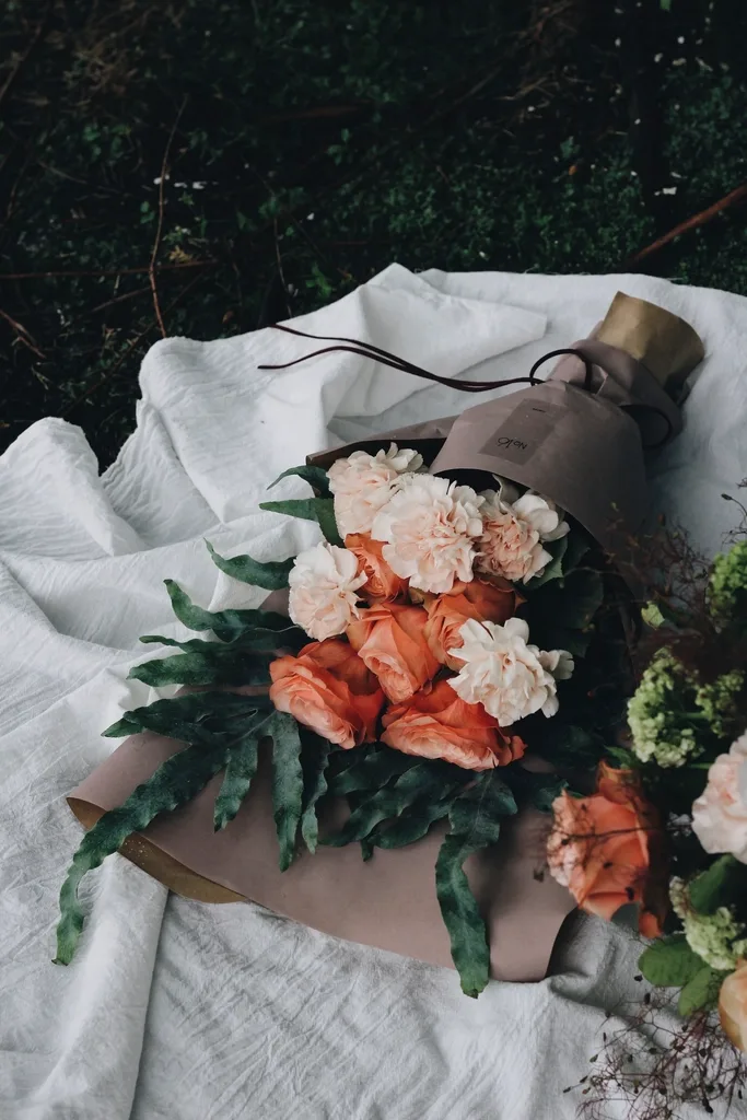 Coral carnations wrapped in paper, resting on linen.